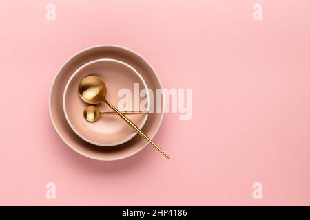 Deux bols à soupe et cuillères sur une table rose, vue du dessus. Couverts dorés pour servir et manger. Jeu de plaques rondes beige. Modèle avec espace de copie pour te Banque D'Images
