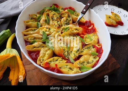 Grandes pâtes en forme de coquille farcies au fromage doux crémeux, courgettes et épinards saupoudrés de parmesan dans un plat de cuisson en bois, dîner sain Banque D'Images