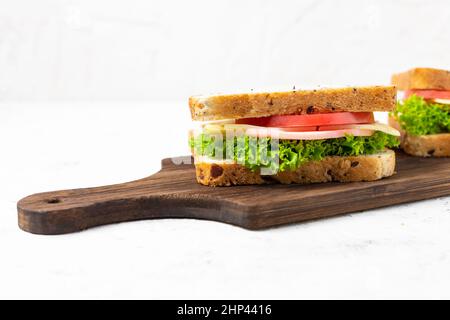 Deux sandwichs avec jambon, fromage, tomates, laitue, oignons. Sandwich maison avec planche à découper de pain à grains entiers sur fond blanc Banque D'Images