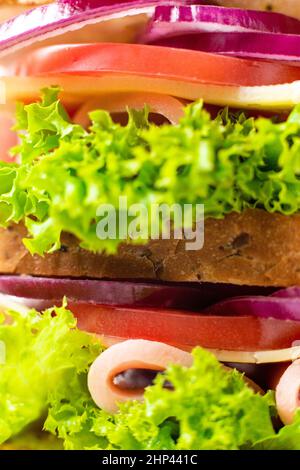 sandwich avec jambon fromage tomates laitue oignons. Macro d'un sandwich multi-couches avec du pain à grains entiers sur fond blanc Banque D'Images