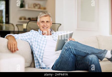 J'ai toujours aimé rester informé des dernières nouvelles Prise de vue d'un homme mûr à l'aide de sa tablette numérique tout en se relaxant sur son canapé à la maison. Banque D'Images