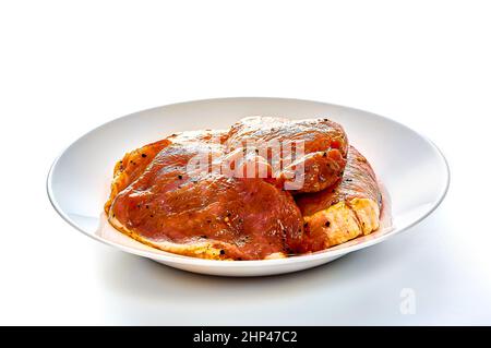 Le porc en marinade repose sur une assiette blanche sur un fond blanc isolé. Photo de haute qualité Banque D'Images