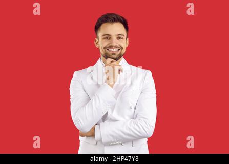 Joyeux beau jeune homme élégant en costume blanc isolé sur fond rouge Banque D'Images