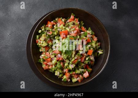 Salade shirazi avec tomates, concombres, oignons rouges, persil et menthe et jus de citron frais dans un bol noir.Salade de légumes shirazi persan en gros plan. Banque D'Images