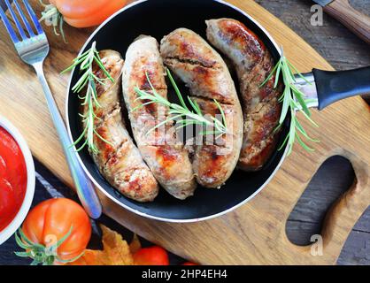 Saucisses grillées sur une poêle avec herbes et épices, fond de bois, gros plan . Banque D'Images