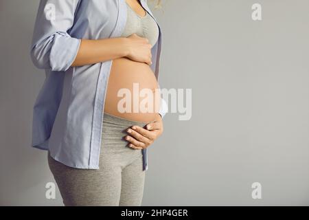 Gros plan du beau ventre de la femme enceinte le neuvième mois debout sur fond gris. Banque D'Images