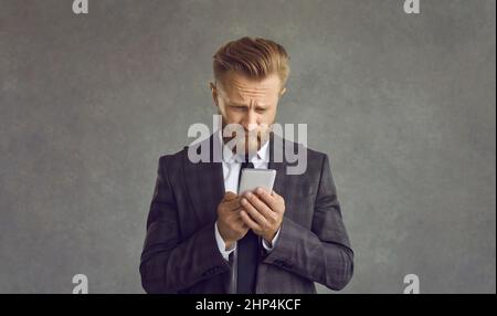 Homme d'affaires malheureux isolé sur fond gris ayant des problèmes avec le téléphone mobile Banque D'Images