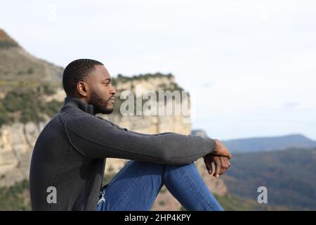 Profil d'un homme sérieux avec une peau noire contemplant assis dans la montagne Banque D'Images