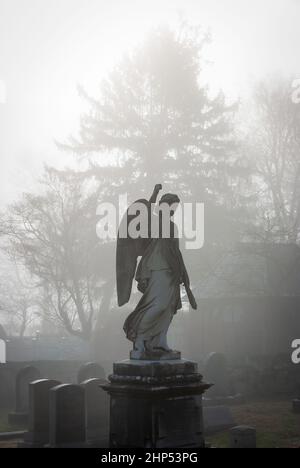 Ange avec cimetière de poing surélevé monument dans le brouillard. Banque D'Images