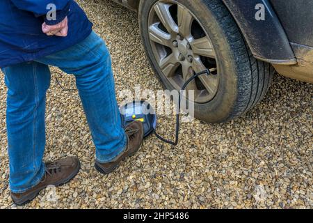 Femme gonflant un pneu sur un SUV à l'aide d'un compresseur d'air portatif à partir de la batterie de la voiture. Banque D'Images