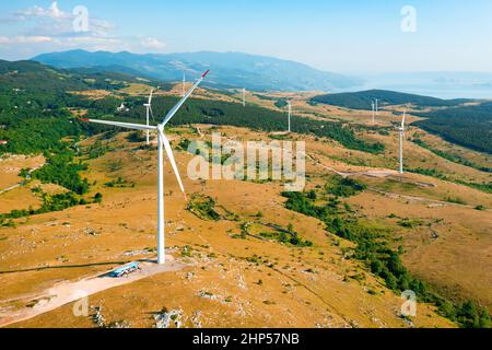 Les éoliennes contemporaines tournent et génèrent de l'énergie propre, diffusée sur les pentes des collines, contre les montagnes forestières, avec une vue aérienne ensoleillée Banque D'Images