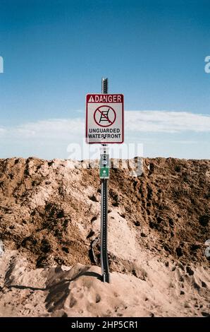 Un panneau de lecture danger non surveillé Waterfront stand devant ce qui semble être un mur de sable. Au lieu de cela, le mur est de neige labourée recouverte d'une couche de Banque D'Images