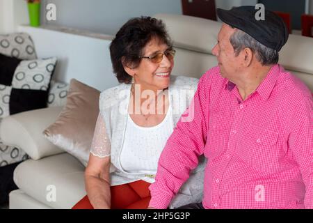 Un vieux couple amoureux se regardant les uns les autres tout en souriant. Vieux couple romantique assis sur leur canapé à la maison. Banque D'Images