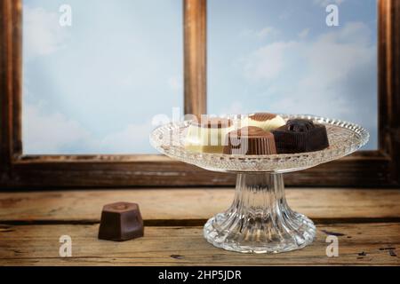 Pralines de chocolat sur une plaque de verre de cristal sur une table rustique en bois devant une fenêtre, espace de copie, foyer sélectionné, profondeur de champ étroite Banque D'Images