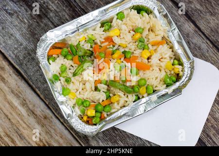 Portion de riz avec légumes mélangés dans un récipient à emporter en papier d'aluminium et couvercle.Sur fond en bois Banque D'Images