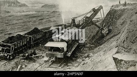 Open Pit Mine d'où vient le minerai. La plus grande partie du minerai de fer extrait en Amérique du Nord provient des mines à ciel ouvert de la région du lac supérieur. Les dépôts sont parfois de trois cents pieds de profondeur et semblent presque inépuisables. Ici, vous voyez une pelle de ruisseau creuser dans la banque et charger les voitures. Une de ces machines fait plus de travail que mille hommes pourraient faire avec des ramasse et des pelles. Banque D'Images