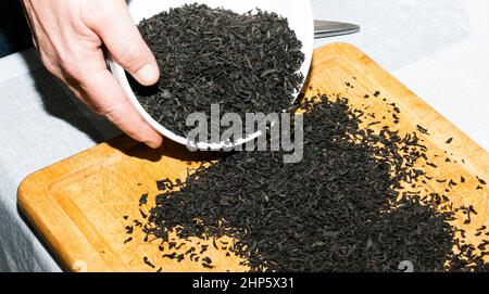 Les mains des femmes saupoudrer de thé noir sur une planche de bois pour sécher. Le processus de fabrication d'un mélange de thé à partir de thé noir, de zeste de citron et d'orange, de morceaux de cinna Banque D'Images