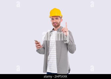 Travailleur de la construction avoir Une idée géniale tenir le téléphone entre les mains. Homme avec idée tenant le doigt vers le haut. Travailleur dans casque dur isolé Banque D'Images