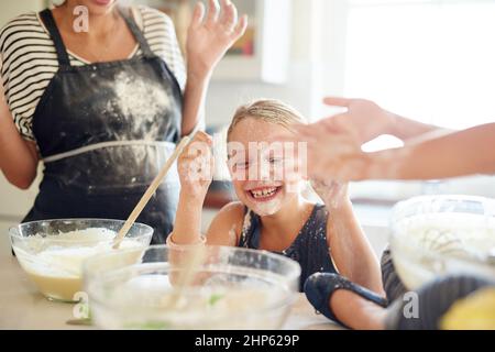 Désordonné mais délicieux. Photo de deux petites filles s'amusant tout en cuisant avec leur mère dans la cuisine. Banque D'Images