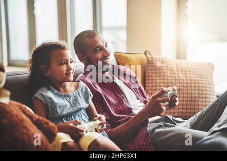 Le gagnant obtient de la crème glacée. Photo d'une adorable petite fille et de son père jouant à des jeux vidéo ensemble sur le canapé à la maison. Banque D'Images