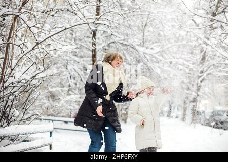 Une grand-mère de famille joyeuse avec des petits-enfants en vêtements chauds jouant à l'extérieur dans le parc d'hiver, profitant du temps gelé et enneigé, les enfants se spe activement Banque D'Images