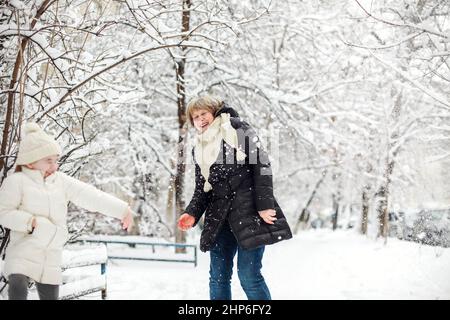 Une grand-mère de famille joyeuse avec des petits-enfants en vêtements chauds jouant à l'extérieur dans le parc d'hiver, profitant du temps gelé et enneigé, les enfants se spe activement Banque D'Images