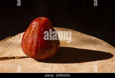 Pommes de rose (Syzygium jambos) sur table en bois avec fond sombre Banque D'Images