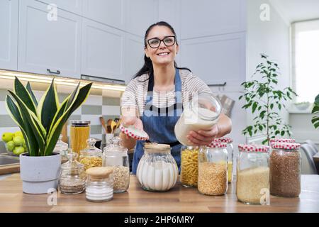 Femme souriante dans la cuisine avec des pots de nourriture stockée. Banque D'Images