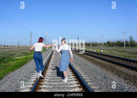 Une adolescente à la main avec une jeune femme marche sur les rails du chemin de fer et garde son équilibre. Banque D'Images