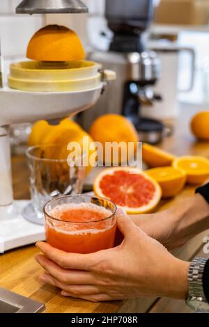 Femme mains avec des oranges mûres entières et à moitié fraîches et des pamplemousses cuisant du jus de détox sur la table Banque D'Images