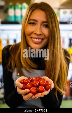 Les mains de la femelle paysanne dans un tablier tenant tas de tomates cerises rouges mûres fraîches en forme de coeur de près Banque D'Images