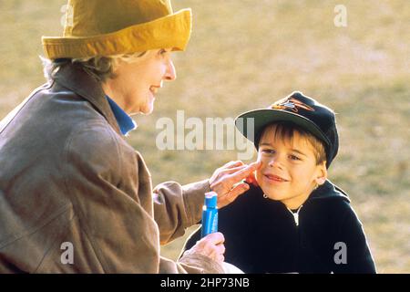 Une femme plus âgée appliquant de la crème solaire à un jeune enfant ca. 1995 Banque D'Images