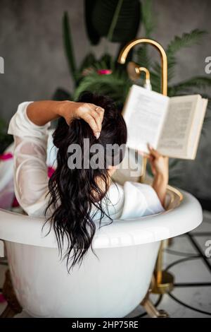 Portrait d'une belle femme posée sur un terrain à carreaux au jardin d'été. Un livre, un fruit, un sac et une pastèque sont à côté l'un de l'autre. Banque D'Images