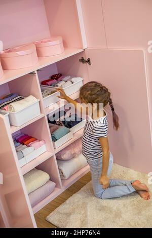 Vue du dessus petite fille a soigneusement plié les vêtements dans la boîte de rangement pour un rangement vertical confortable sur les étagères Banque D'Images