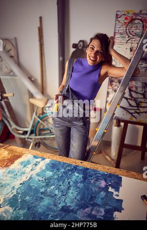 Femme souriante dessinant sur une toile dans un studio d'art.ambiance créative. Banque D'Images