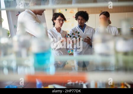 Les jeunes étudiants en chimie prennent des notes et discutent du modèle moléculaire dans une atmosphère détendue dans le laboratoire universitaire. Science, chimie, laboratoire, personnes Banque D'Images