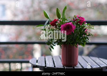 Un beau bouquet de roses rouges et violettes dans un vase sur une table à l'extérieur Banque D'Images