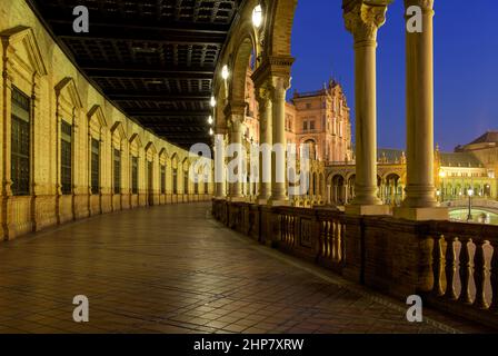 Spanish Square - vue panoramique au crépuscule sur le portique lumineux situé au rez-de-chaussée, le long d'un bâtiment en brique semi-circulaire sur la place espagnole, Séville, Espagne. Banque D'Images