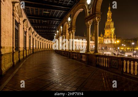 Place de l'Espagne - vue nocturne du portique lumineux situé au rez-de-chaussée, longeant le bâtiment en briques semi-circulaires de la place de l'Espagne, Séville, Espagne. Banque D'Images