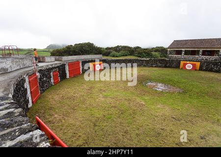 Garçon regardant l'arène rurale vierge de tauromachie dans la campagne de l'île de Terceira dans les Açores, faite de pierres volcaniques une porte rouge Banque D'Images