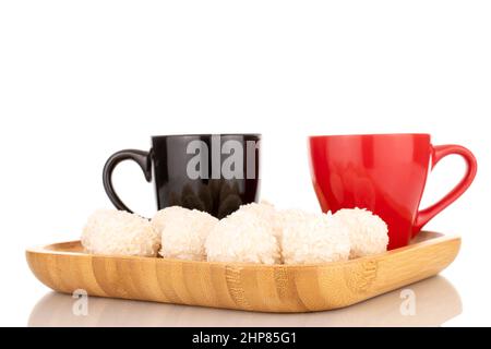 Quelques sucreries de noix de coco sucrées sur un plateau de bambou avec deux tasses, macro, isolé sur un fond blanc. Banque D'Images