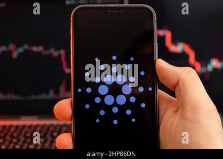 Application Cardano ADA de l'analyse du marché des actions de crypto-monnaie sur l'écran du téléphone mobile dans les mains de l'homme et des graphiques de tendance à la baisse des données de négociation sur le fond, février 2022, San Francisco, États-Unis. Banque D'Images