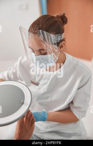 Jeune femme avec écran facial travaille avec l'homme pied à la procédure de pédicure dans le salon Banque D'Images