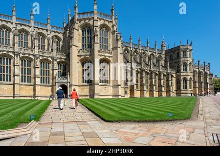 Deux visiteurs marchent le long de la voie en passant devant des pelouses soignées jusqu'à l'entrée de la chapelle Saint-Georges située dans la partie inférieure du château de Windsor, dans le Berkshire Banque D'Images