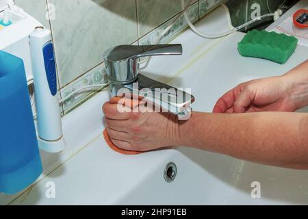 Le processus de nettoyage quotidien de l'évier avec de la poudre à laver et un chiffon ménager. Une femme au foyer à la main sans gants nettoie le robinet d'eau nettoie votre h Banque D'Images