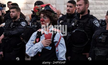 Un activiste israélien portant un costume de police et le nez rouge d'un clown se tient parmi les policiers pendant qu'ils regardent pendant une manifestation tenue par des activistes de gauche et des Palestiniens contre l'occupation israélienne et les activités de colonisation dans le quartier de Sheikh Jarrah le 18 février 2022 à Jérusalem, en Israël. Le quartier palestinien de Sheikh Jarrah est actuellement au centre d'un certain nombre de conflits de propriété entre Palestiniens et Israéliens juifs de droite. Certaines maisons ont été occupées par des colons israéliens à la suite d'une décision du tribunal. Banque D'Images