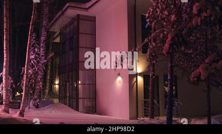 Façade de la grande maison à la fin de la soirée d'hiver illuminée par la lumière clignotante colorée d'une voiture de secours. Vue à l'extérieur du cottage dans la neige Banque D'Images