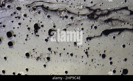 Vue de dessus des gouttes d'encre noire qui s'écoulent dans l'huile liquide sur fond gris métallique.Boules noires de peinture flottant sur la surface de la substance huileuse Banque D'Images