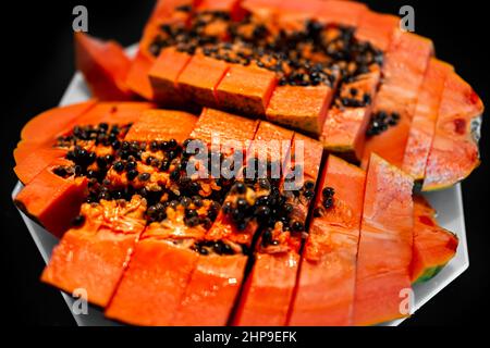 Gros plan macro de grands fruits de papaye mûrs rouge des Caraïbes tranchés deux tranches de deux moitiés avec de la chair fraîche orange rouge colorée coupée en deux sur l'assiette avec b noir Banque D'Images