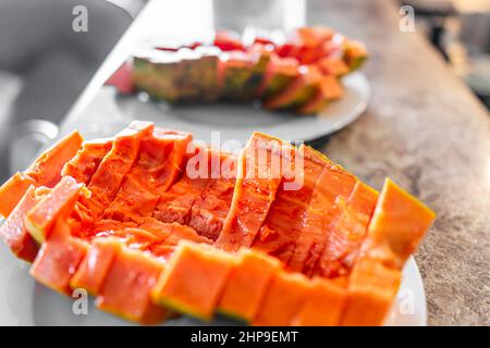 Gros plan de grands fruits de papaye mûrs rouge des Caraïbes tranchés avec chair fraîche orange rouge colorée coupée en deux sur le comptoir de bar avec deux assiettes pour le romantique t Banque D'Images